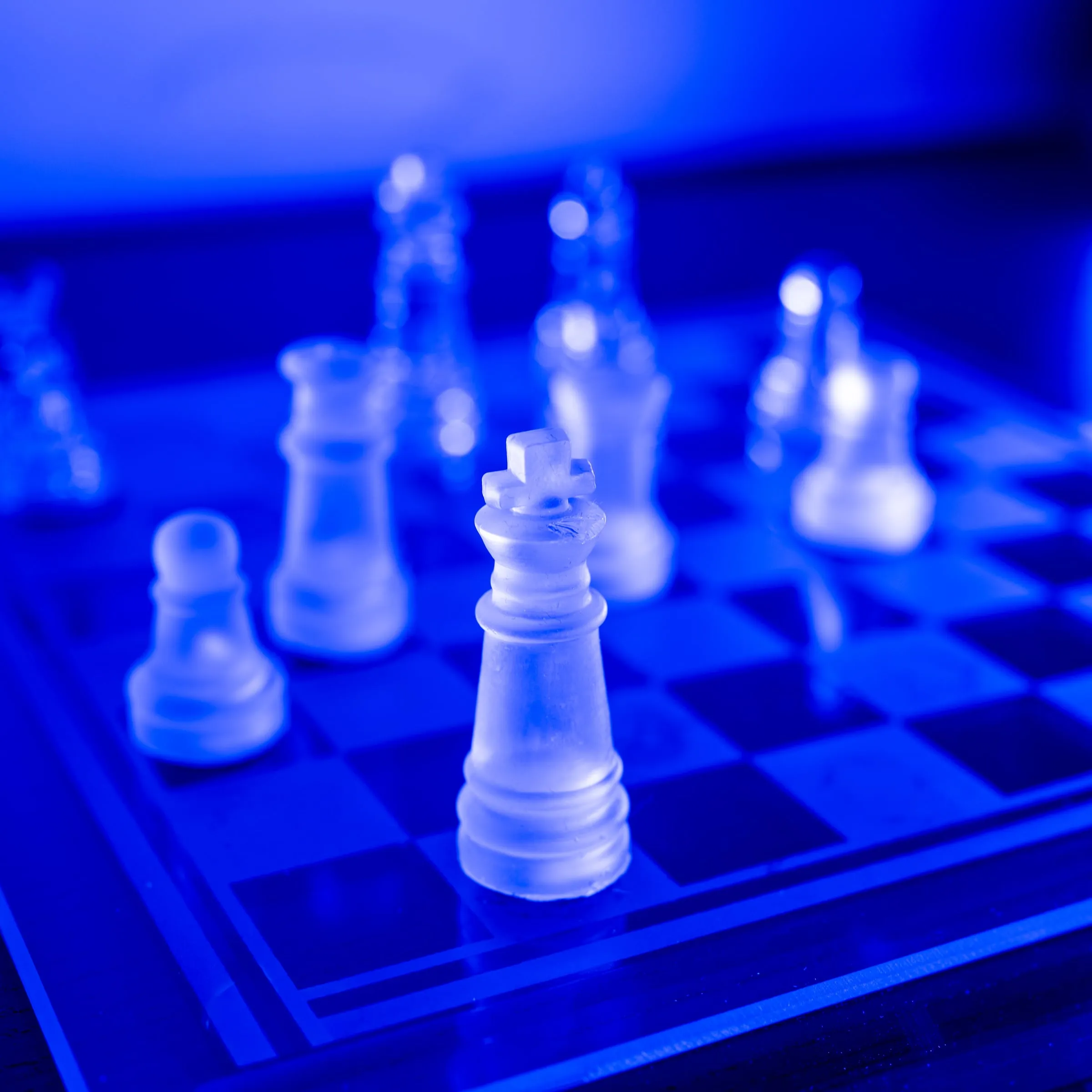 Gläserne Schachfiguren auf einem Brett in blauem Licht – der König scharf im Vordergrund